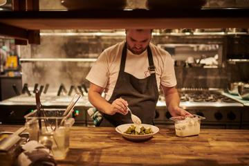 Chef serving a bowl of green food in kitchen of Astoria.