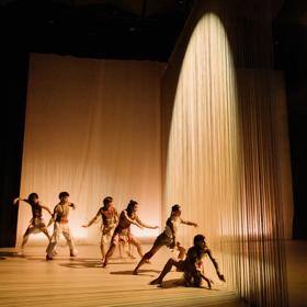 Dances perform on a stage, bathed in golden light as part of Ka Mua Ka Muri.