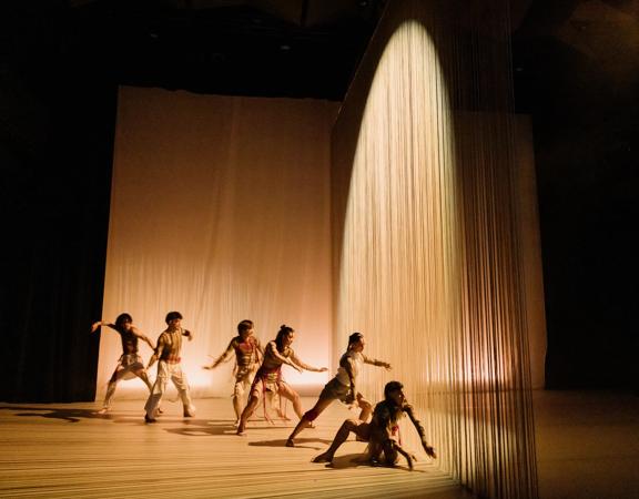 Dances perform on a stage, bathed in golden light as part of Ka Mua Ka Muri.