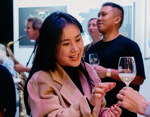 A person looking at a glass of wine being poured for them, smiling.