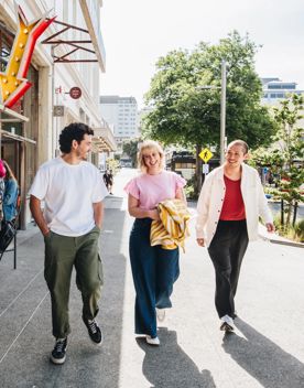 Three people walk along Swan Lane in Te Aro, Wellington, beside an open café on a sunny day.