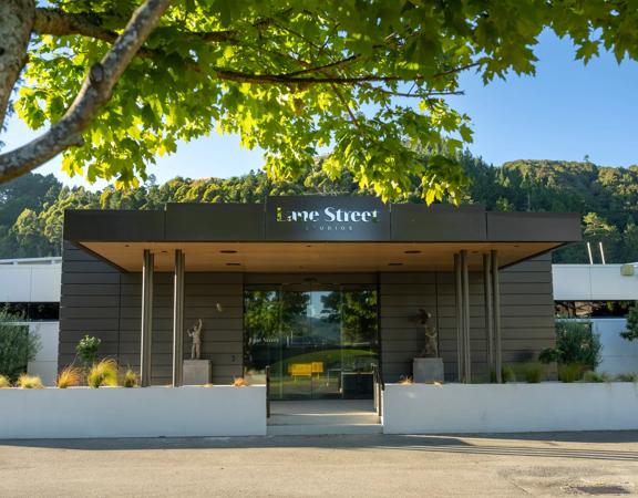 The front exterior of Lane Street Studios in Upper Hutt. A veranda with a name sign sits over the glass front doors. White planter boxes sit out front.