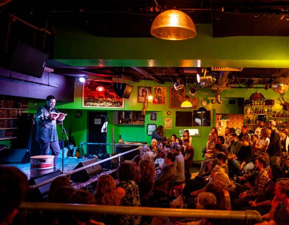 A person on stage with a microphone reads a book to a packed audience at the Verb Readers and Writers Festival in Wellington.