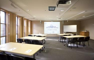 A conference room set up with five tables with three chairs at each facing a screen projector and a white board.