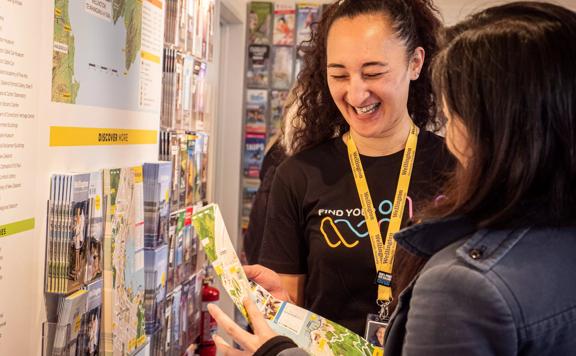 A team member from the isite helps a customer look at a map of Wellington, and they share a laugh.