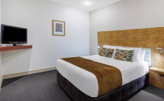 A bedroom at CityLife Hotel features a bed with crisp white sheets against a wooden headboard with a TV in the opposite corner.