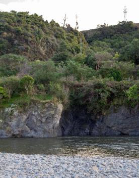 The Taitā Rock swimming hole in Lower Hutt, with lush green bush surrounding a blue river and large pebbles on the shore.