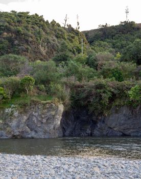 The Taitā Rock swimming hole in Lower Hutt, with lush green bush surrounding a blue river and large pebbles on the shore.