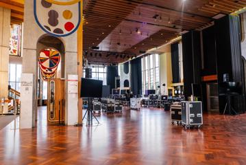 Inside a large foyer space with hardwood floors, cases of audio and lighting equipment everywhere and floor-to-ceiling windows.