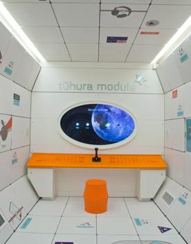 Inside the Tūhura module at Space Place, a room set up like the inside of a spaceship with white walls and a control panel.