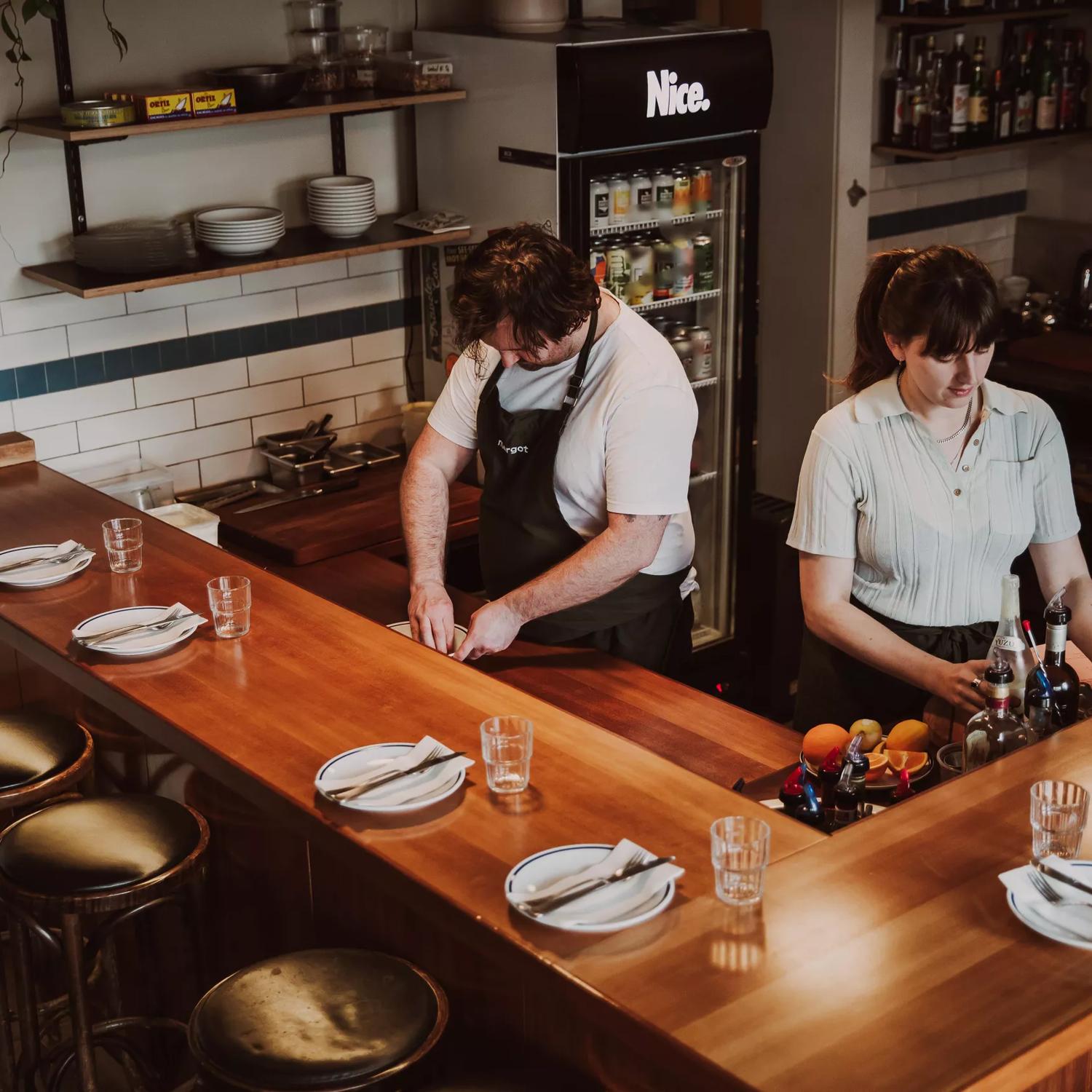 2 staff members preparing food inside Margot on a wooden bar.