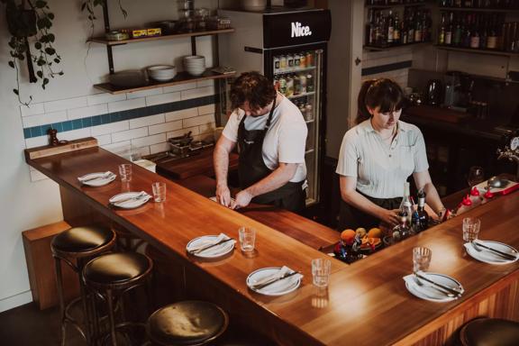 2 staff members preparing food inside Margot on a wooden bar.