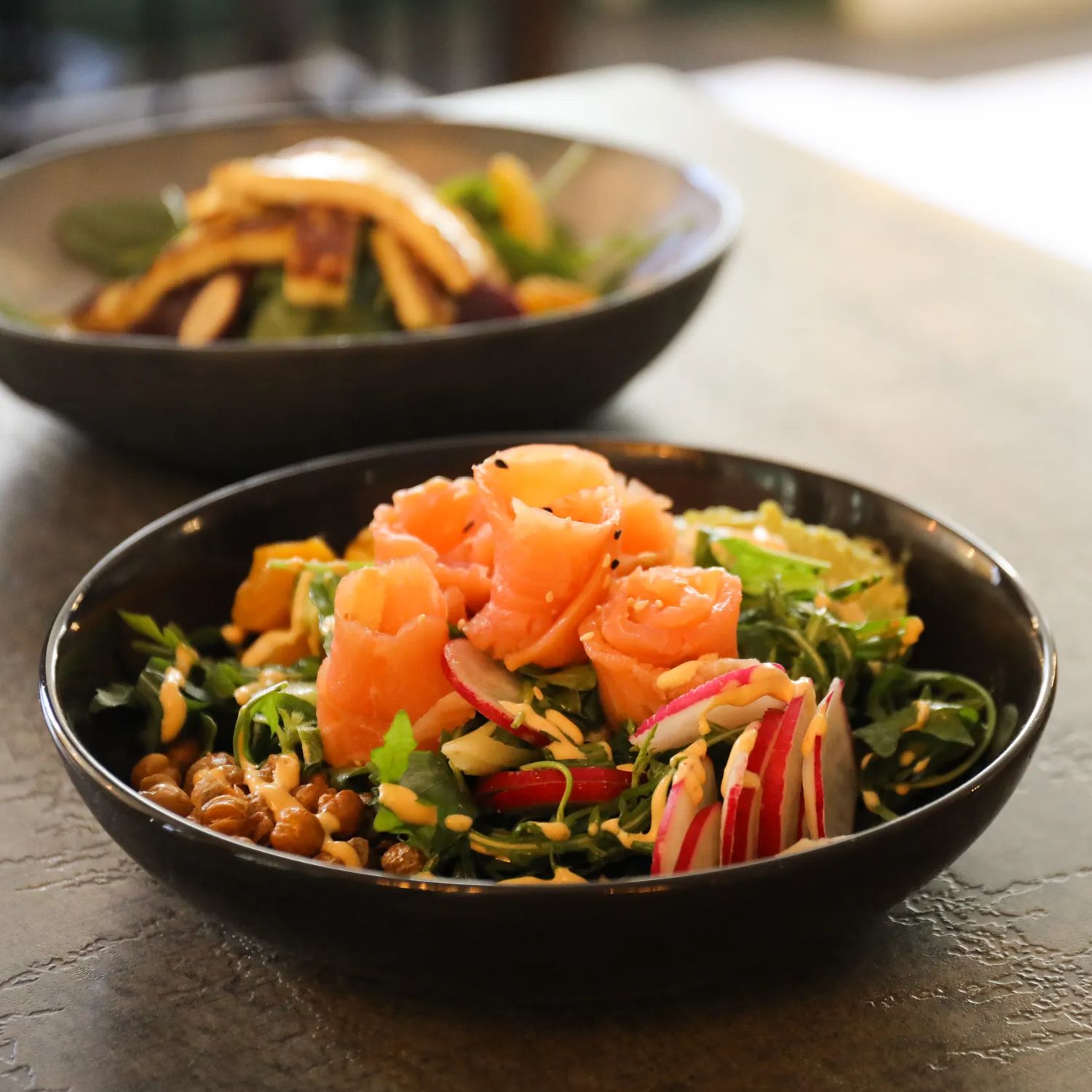 Fresh salad with smoked salmon in a black bowl on a restaurant table.