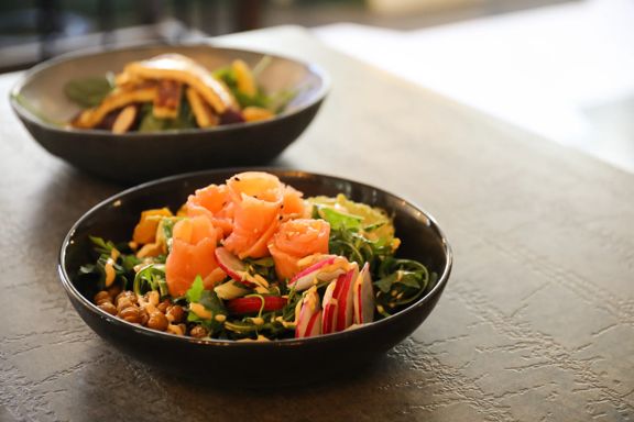 Fresh salad with smoked salmon in a black bowl on a restaurant table.
