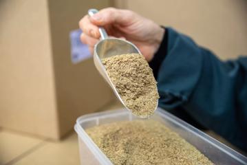 A hand using a silver scoop of pick-up ground grain.