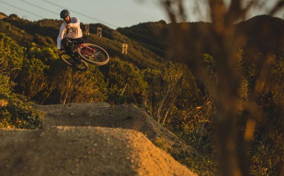 A mountain biker jumps over a dirt mound on the Super Plus trail in Wainuiomata.