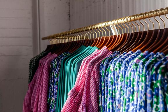 Colour coordinated clothing on wood and gold hangers lined perfectly on a rack in Twenty Seven Names.