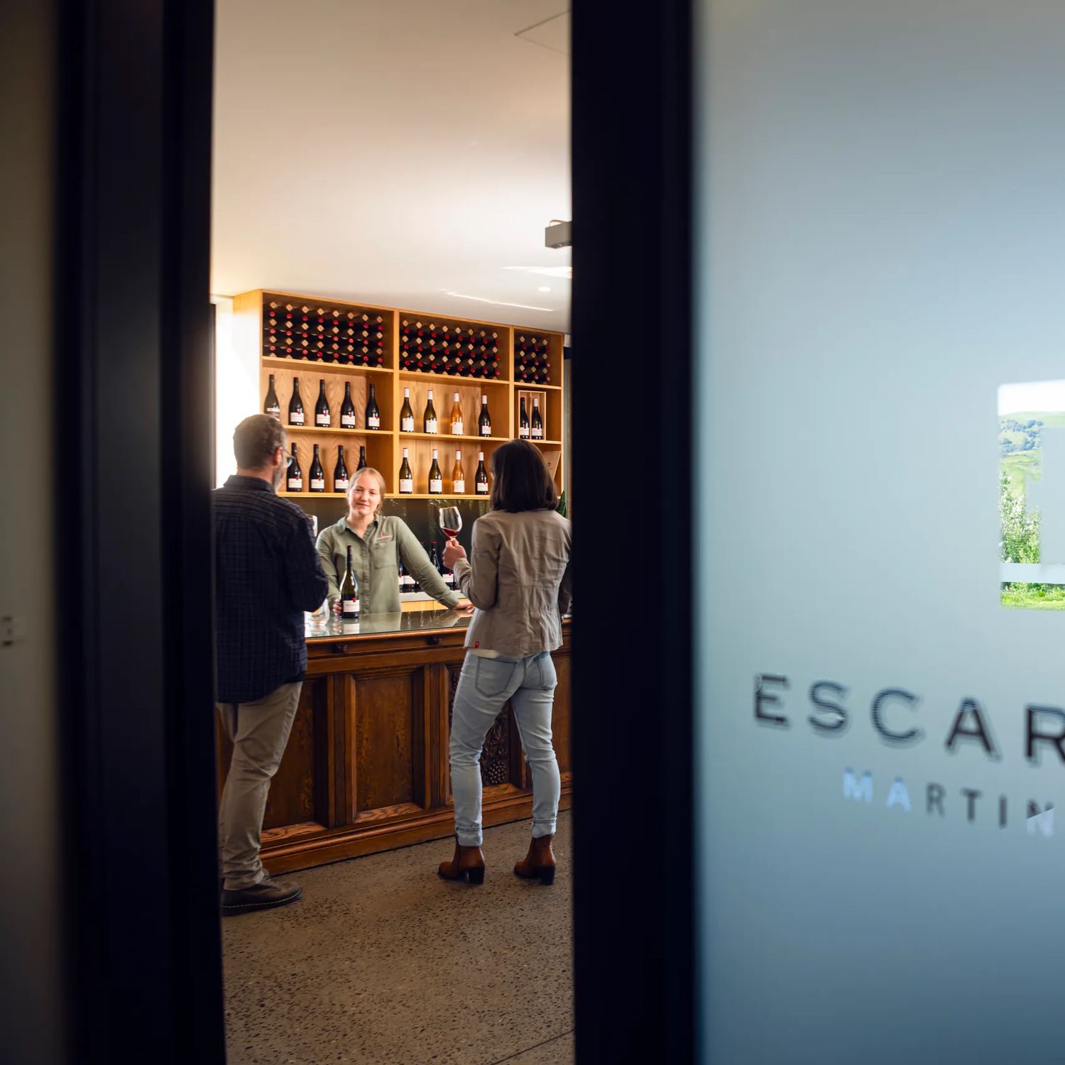Looking through the door at Escarpment Winery in Wairarapa, where two people are wine tasting.