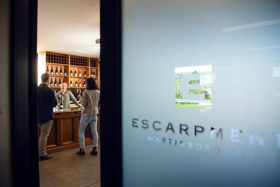 Looking through the door at Escarpment Winery in Wairarapa, where two people are wine tasting.