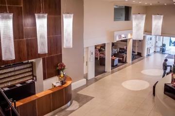 West Plaza Hotel lounge and lobby space with high ceilings, cylindrical chandeliers and beige tiled floor.