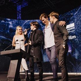 Four people standing at a podium on stage at the New Zealand Youth Film Festival.