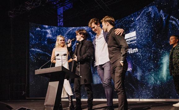 Four people standing at a podium on stage at the New Zealand Youth Film Festival.