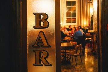 The doorway into Puffin wine bar inside the Intrepid Hotel in Wellington. The frosted window on the door says "BAR" and patrons are sitting at tables inside the amber-lit space.