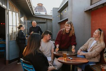 Waitstaff sets down two wine glasses in front of customers in the outside patio of Ascot.