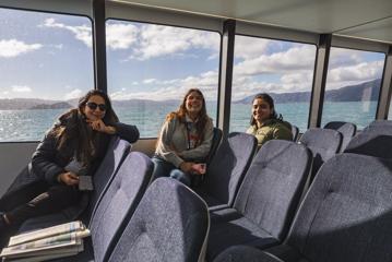 Three people sit on an East by West Ferry in Wellington, New Zealand.