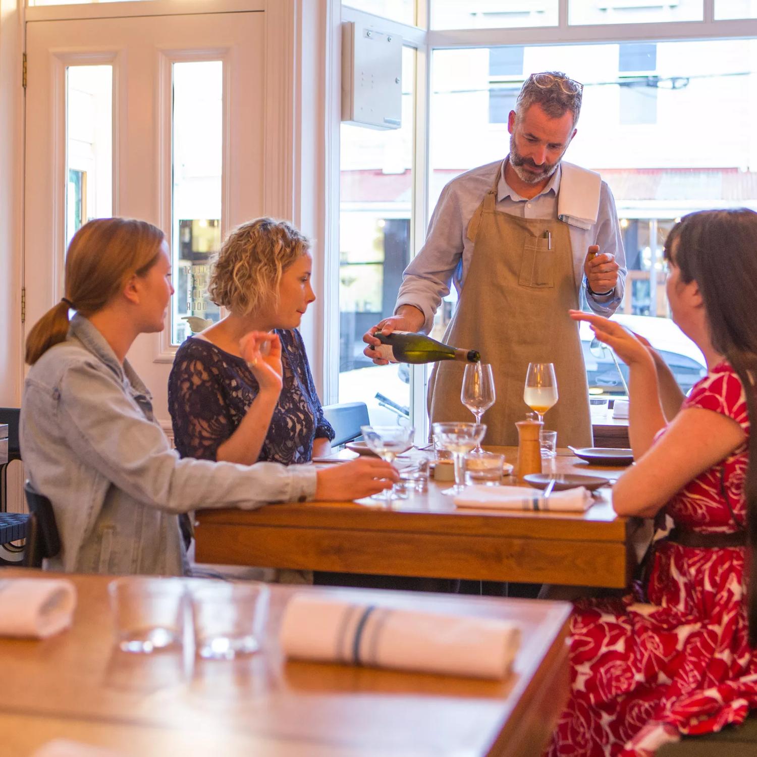 The waitstaff pouring a glass of wine for a table with 4 customers. inside Rita in Aro Valley.