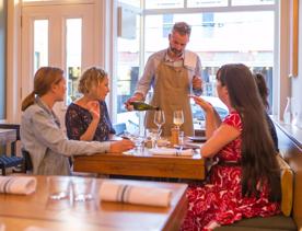 The waitstaff pouring a glass of wine for a table with 4 customers. inside Rita in Aro Valley.