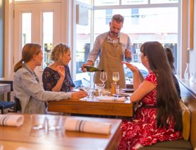 The waitstaff pouring a glass of wine for a table with 4 customers. inside Rita in Aro Valley.
