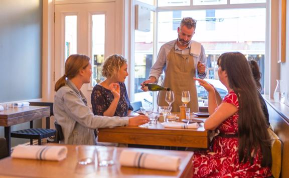 The waitstaff pouring a glass of wine for a table with 4 customers. inside Rita in Aro Valley.