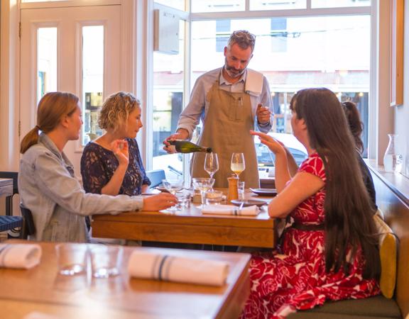 The waitstaff pouring a glass of wine for a table with 4 customers. inside Rita in Aro Valley.