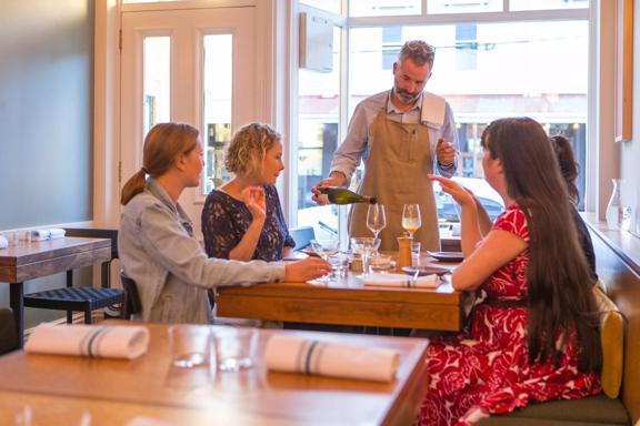 The waitstaff pouring a glass of wine for a table with 4 customers. inside Rita in Aro Valley.