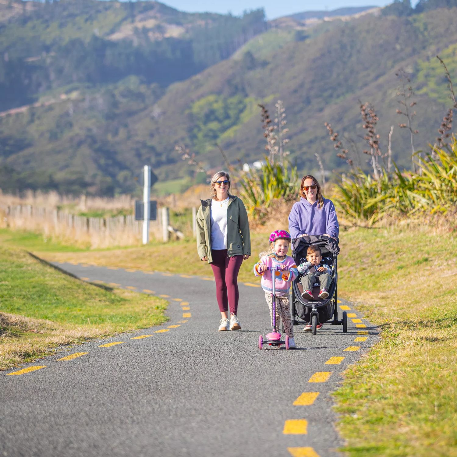 Two parents walking their children on Te ara o Whareroa trail. One child is in a pram and one is riding a scooter.