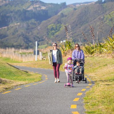 Two parents walking their children on Te ara o Whareroa trail. One child is in a pram and one is riding a scooter.