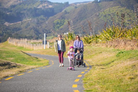 Two parents walking their children on Te ara o Whareroa trail. One child is in a pram and one is riding a scooter.