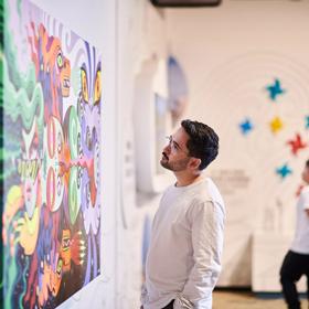 The interior of Te Whanganui-a-Tara exhibition at the Wellington Museum with two people admiring the colourful artwork displayed. 