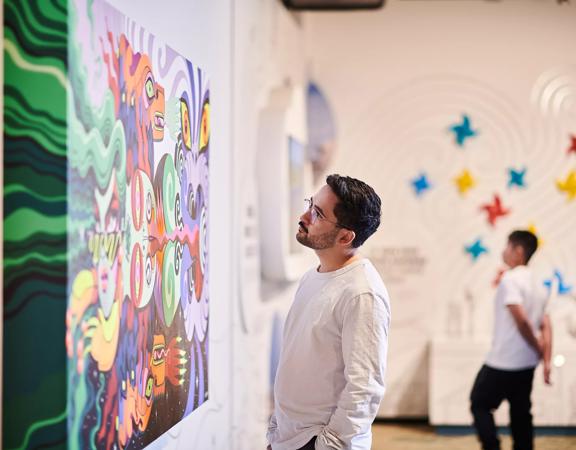 The interior of Te Whanganui-a-Tara exhibition at the Wellington Museum with two people admiring the colourful artwork displayed. 