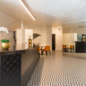 Inside the open, minimal-styled lobby at Bay Plaza Hotel, with turmeric-coloured chairs, a tiled floor and a mirror wall across from the front desk.