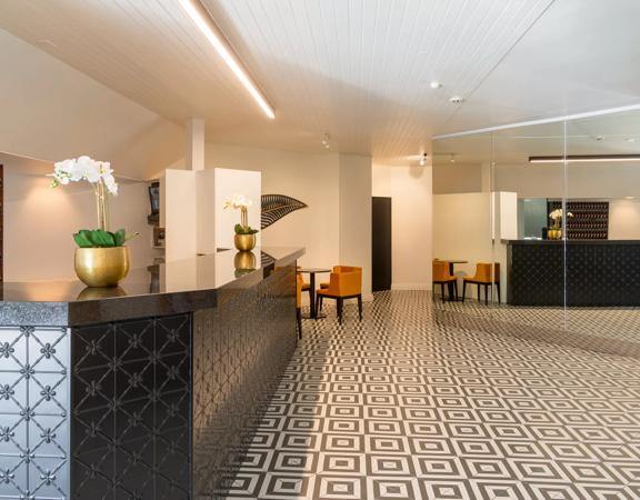 Inside the open, minimal-styled lobby at Bay Plaza Hotel, with turmeric-coloured chairs, a tiled floor and a mirror wall across from the front desk.