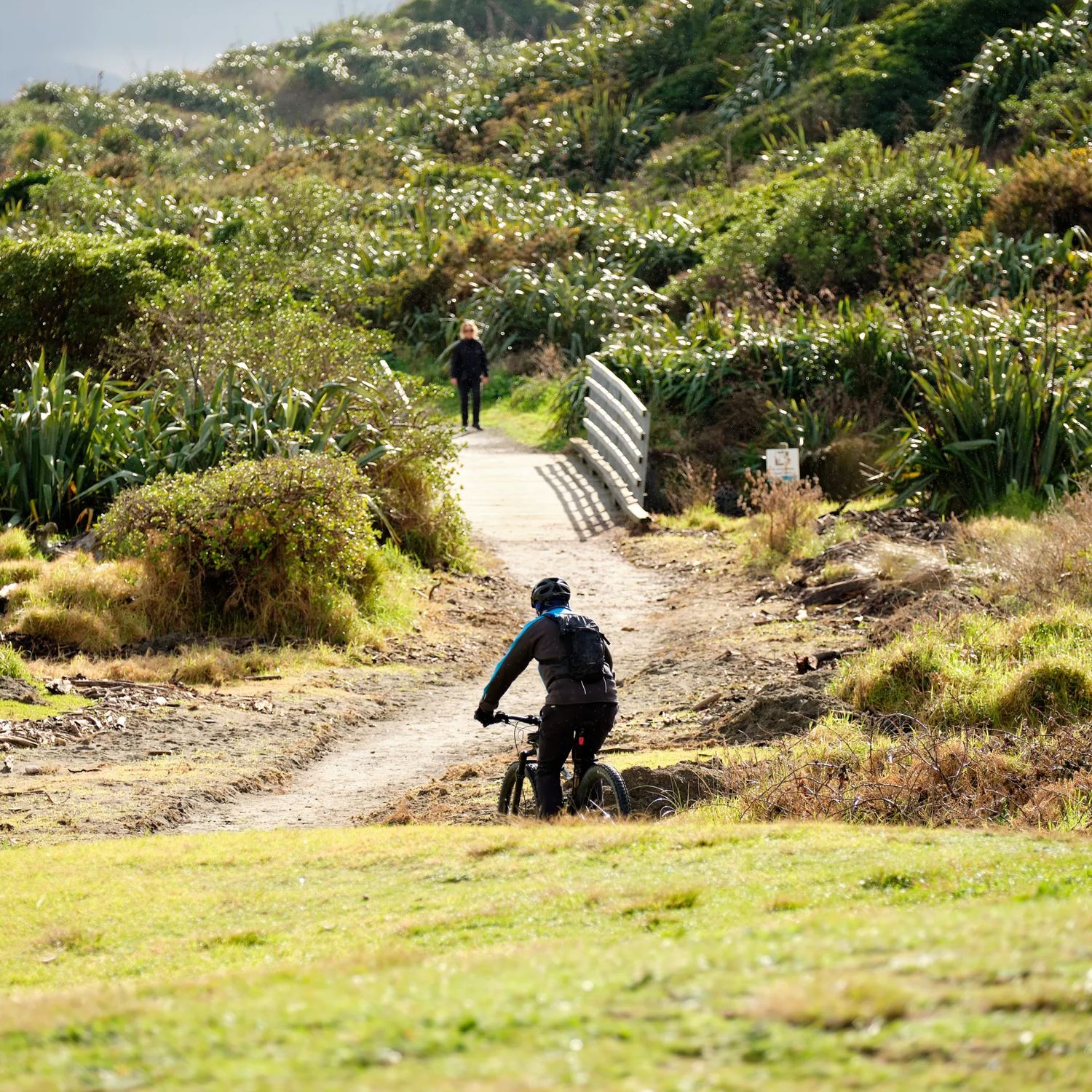 A cyclist rides along the Coastal Track at Queen Elizabeth Park towards a small bridge.
