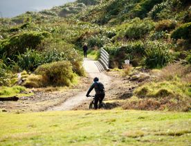 A cyclist rides along the Coastal Track at Queen Elizabeth Park towards a small bridge.