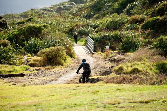 A cyclist rides along the Coastal Track at Queen Elizabeth Park towards a small bridge.