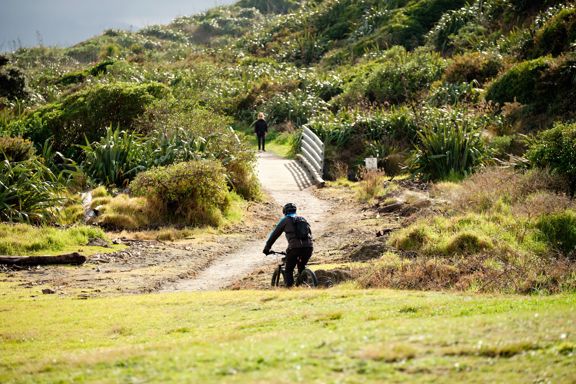 A cyclist rides along the Coastal Track at Queen Elizabeth Park towards a small bridge.