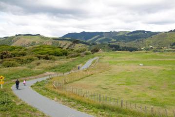 Two children and an adult cycling along a long, flat, gravel path in Queen Elizabeth Park with hills in the background..