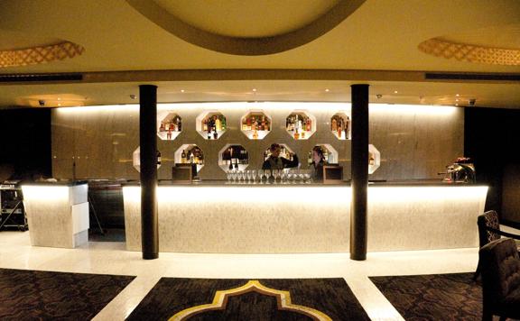 A bar with two workers standing behind the counter, wine glasses lined up on the bar.