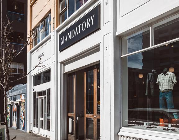 The front facade of Mandatory Menswear Ltd, a men's clothing store in Te Aro, Wellington. It's a white building with wood-framed doors and large windows.