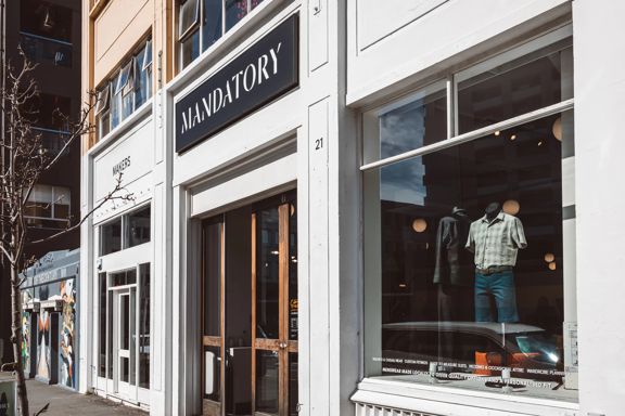 The front facade of Mandatory Menswear Ltd, a men's clothing store in Te Aro, Wellington. It's a white building with wood-framed doors and large windows.
